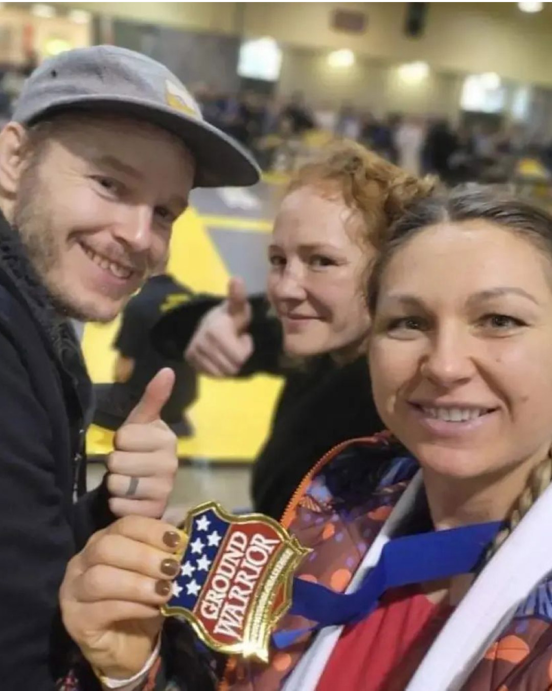 A woman and her friends pose for a photo with her Ground Warrior metal after a tournament. They are smiling and happy.