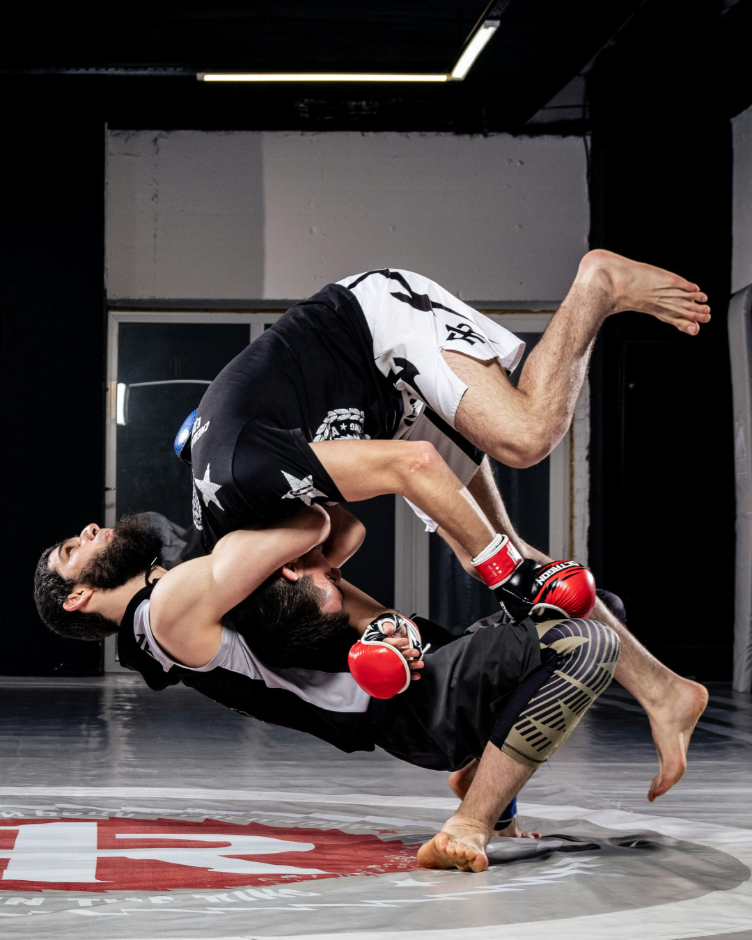A man performs a suplex on another male during a grappling sessions. They both wear black tops.