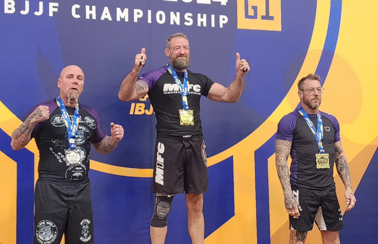 Three men stand on a podium after competing in a jiu-jitsu tournament.