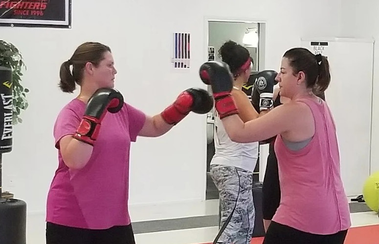 Two woman wearing pink with pony tails practice throwing punches in a cardio kickboxing class